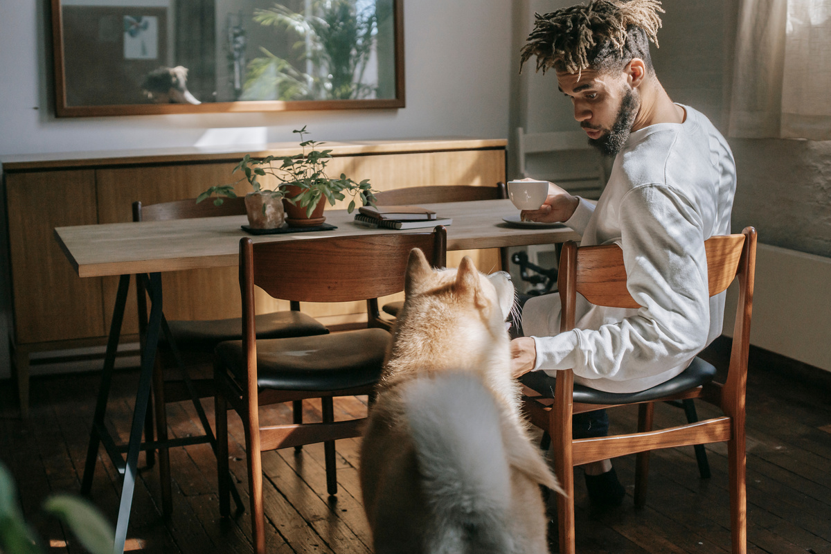 African American man petting cute dog while drinking coffee at home